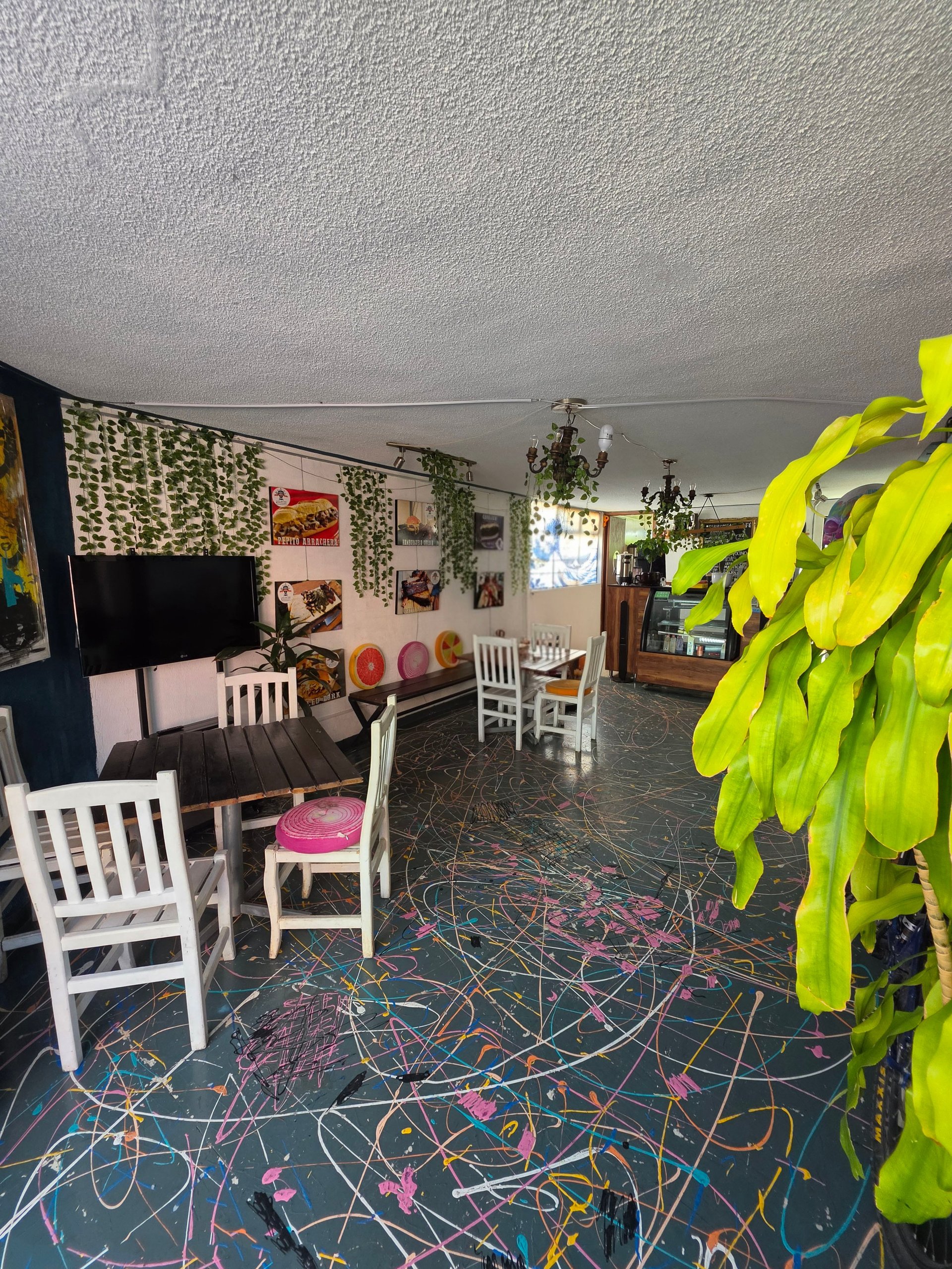 Indoor art studio with colorful painted floor, white chairs, potted plants, and artwork on walls