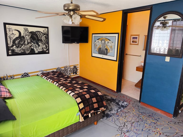Colorful bedroom with bright green bed, yellow accent wall, blue door, ceiling fan, and eclectic artwork on walls