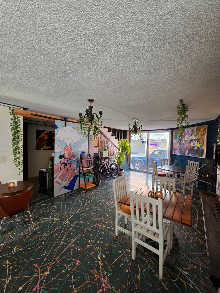 Artistic loft space with textured ceiling, hanging plants, colorful murals on walls, white chairs, and abstract patterned floor.