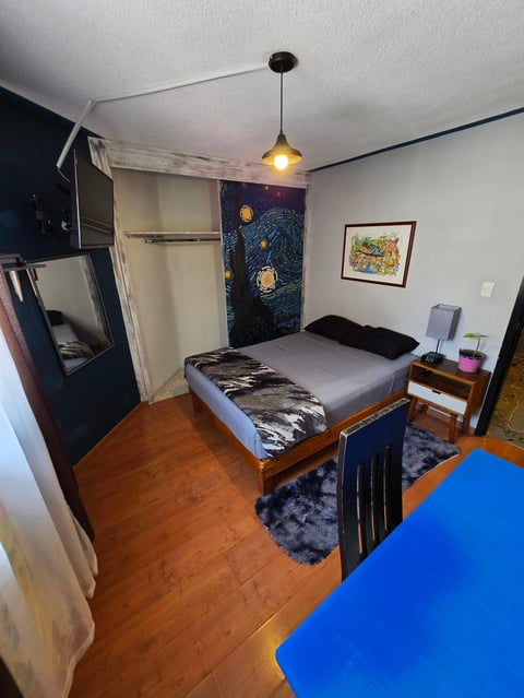 Cozy bedroom with wood flooring, single bed, dark blue accents, hanging pendant light, and small nightstand with storage.