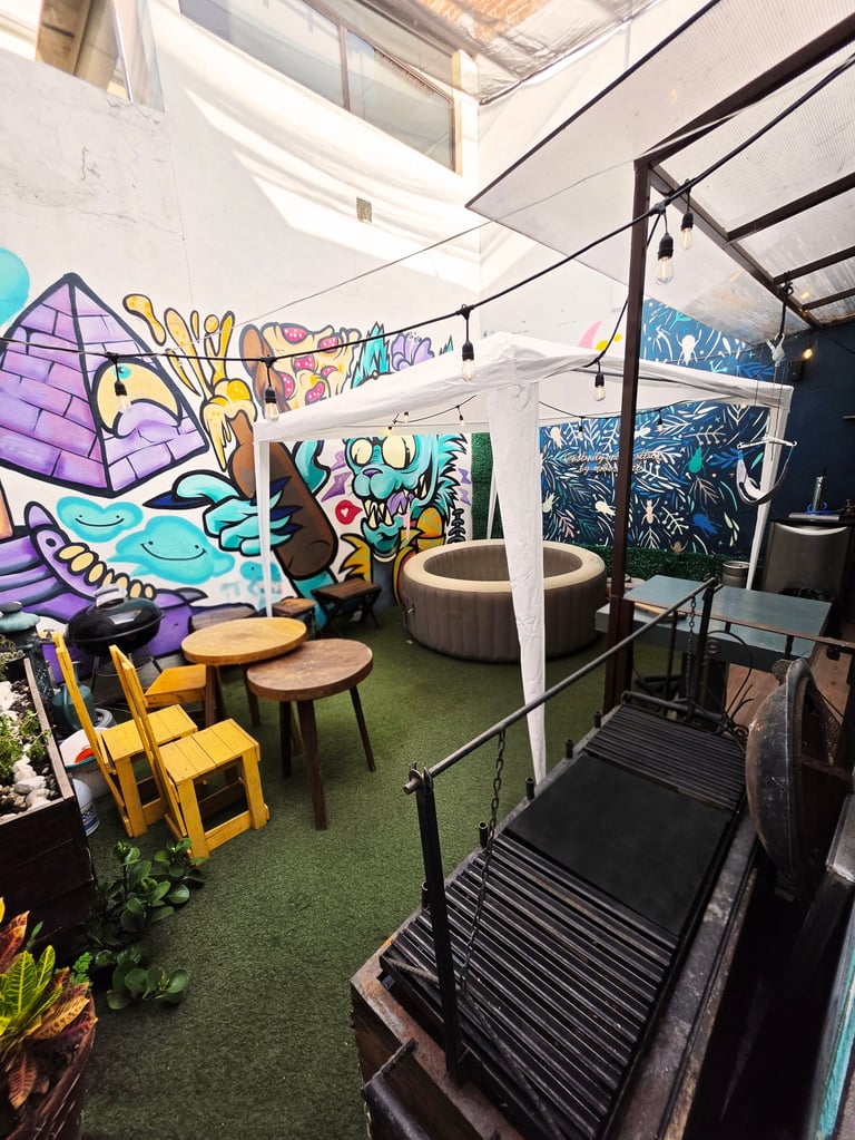 Colorful indoor art gallery space with vibrant graffiti murals, yellow chairs, round seating areas, artificial grass flooring, and skylight ceiling.
