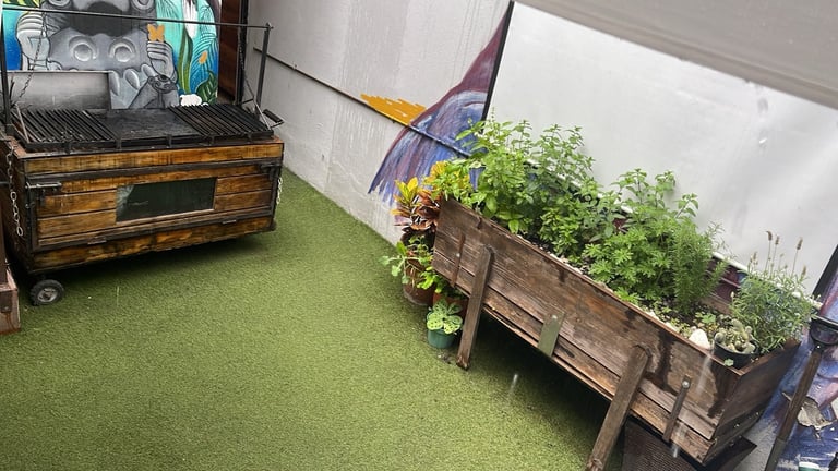 Indoor garden setup with wooden raised beds containing green plants on artificial turf floor next to storage box