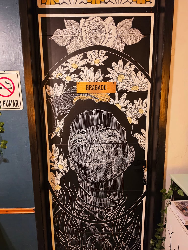 Black and white portrait artwork with orange accents featuring a person surrounded by detailed floral designs and a yellow banner reading GRABADO