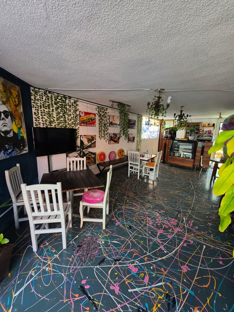 Colorful art studio or creative space with white chairs, wall art, hanging plants, and a black floor decorated with colorful scribbles