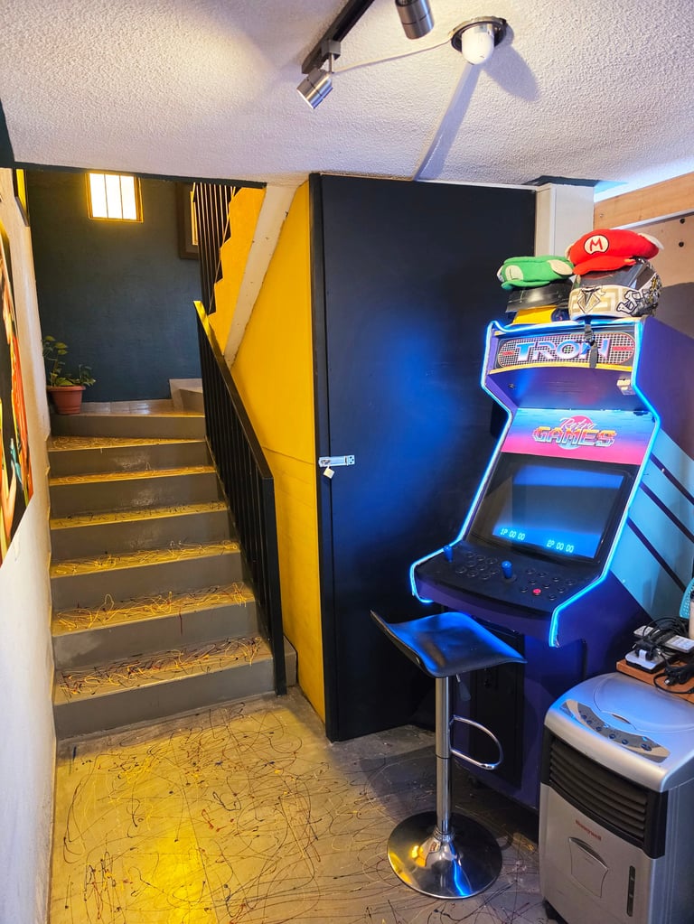 Game room with staircase, yellow flooring, neon-lit arcade machine with Mario hat, and blue wall backdrop