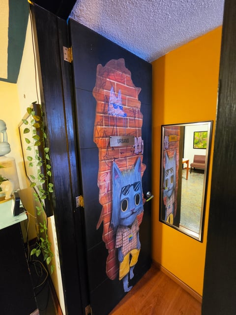 Colorful hallway with yellow walls, black door featuring cartoon character artwork, and mirror on orange wall
